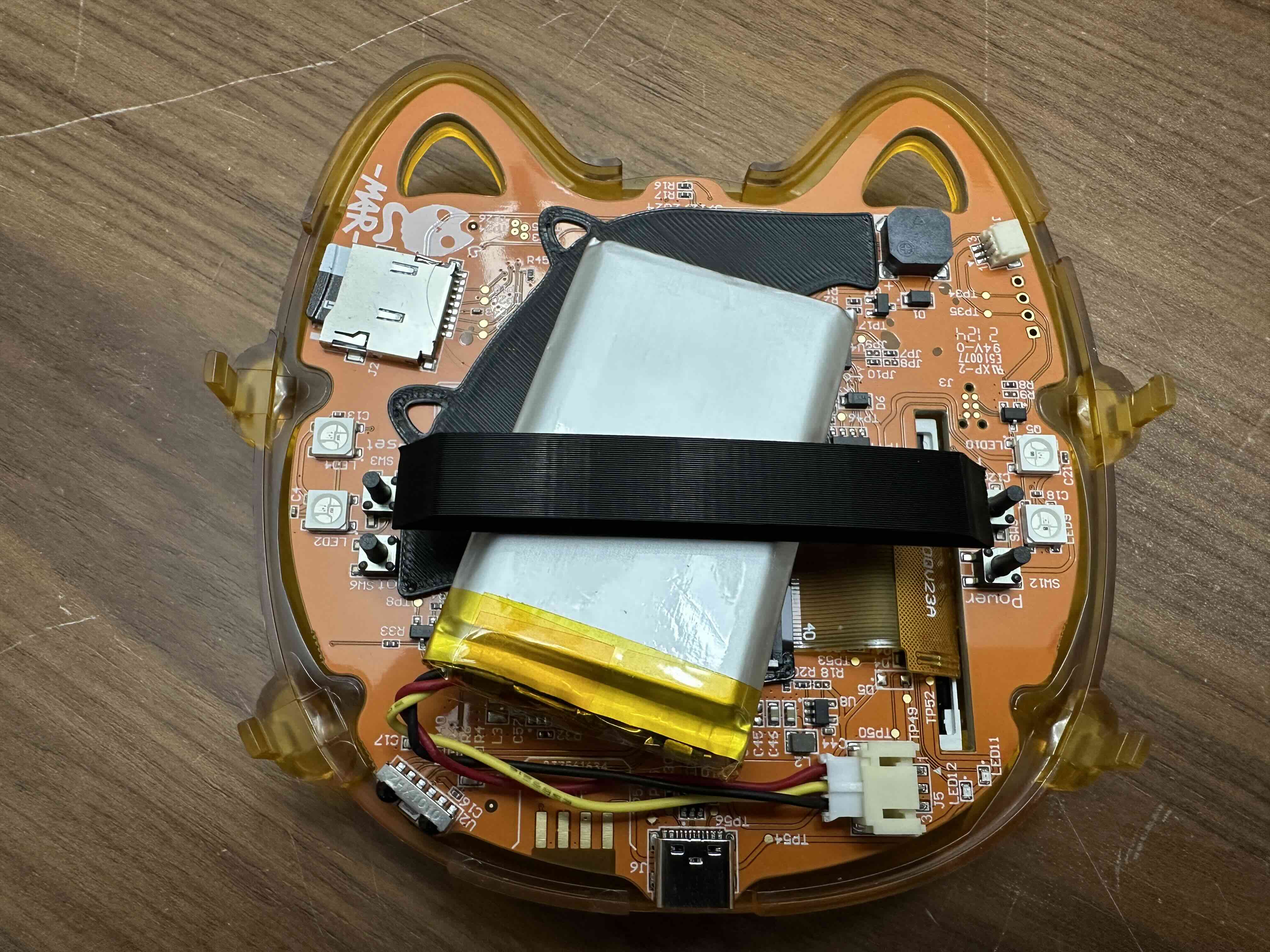 Yellow vendor badge showing squishy band resting on top of battery as if connecting the buttons on each side. Cover not yet installed.